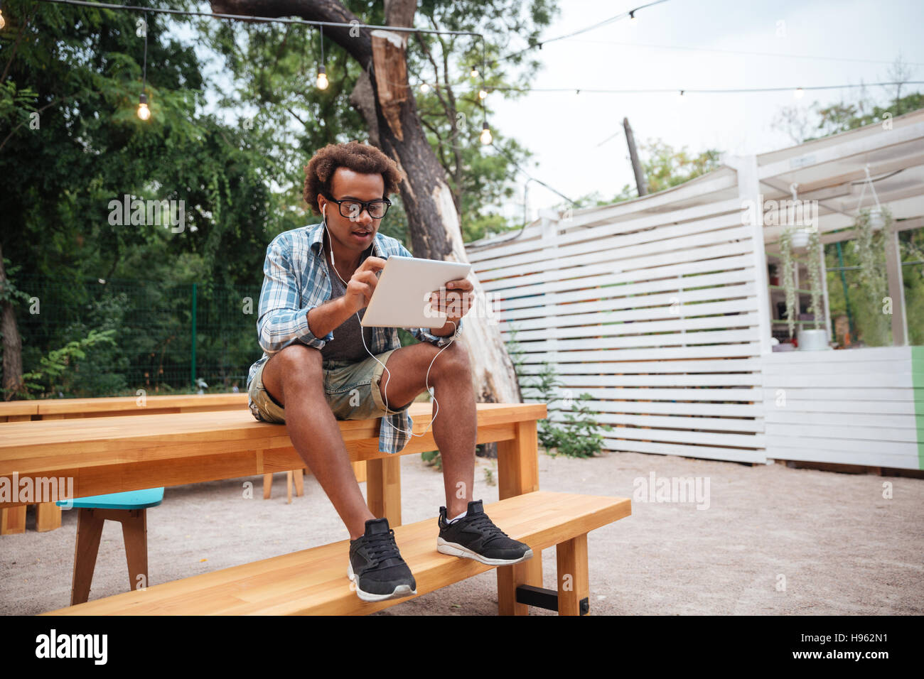 Hübscher afroamerikanische junger Mann in Gläsern mit Tablet sitzen im park Stockfoto