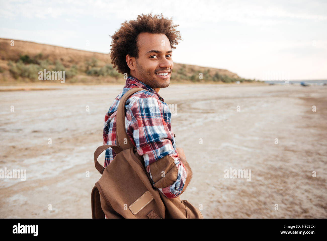 Lächelnd afroamerikanischen jungen Mann mit Rucksack zu Fuß am Strand Stockfoto