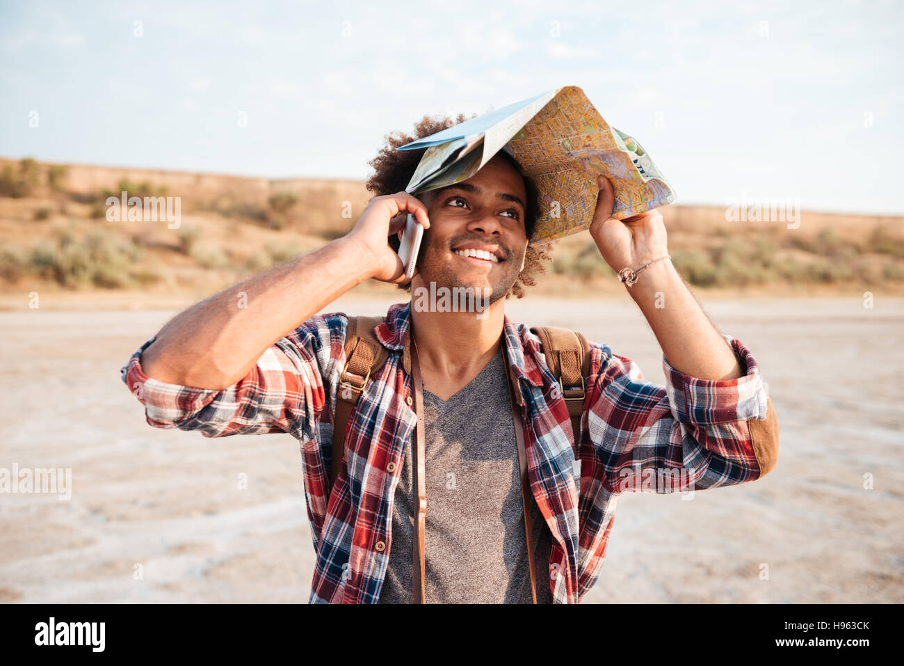 Glücklicher afroamerikanischer jungen Mann bedeckt Kopf mit Karte und reden über Handy Stockfoto