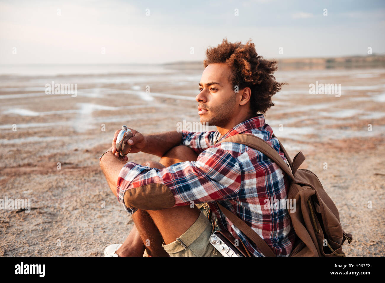 Nachdenklich afrikanischen jungen Mann mit Rucksack sitzen und Trinken von Flachmann Stockfoto