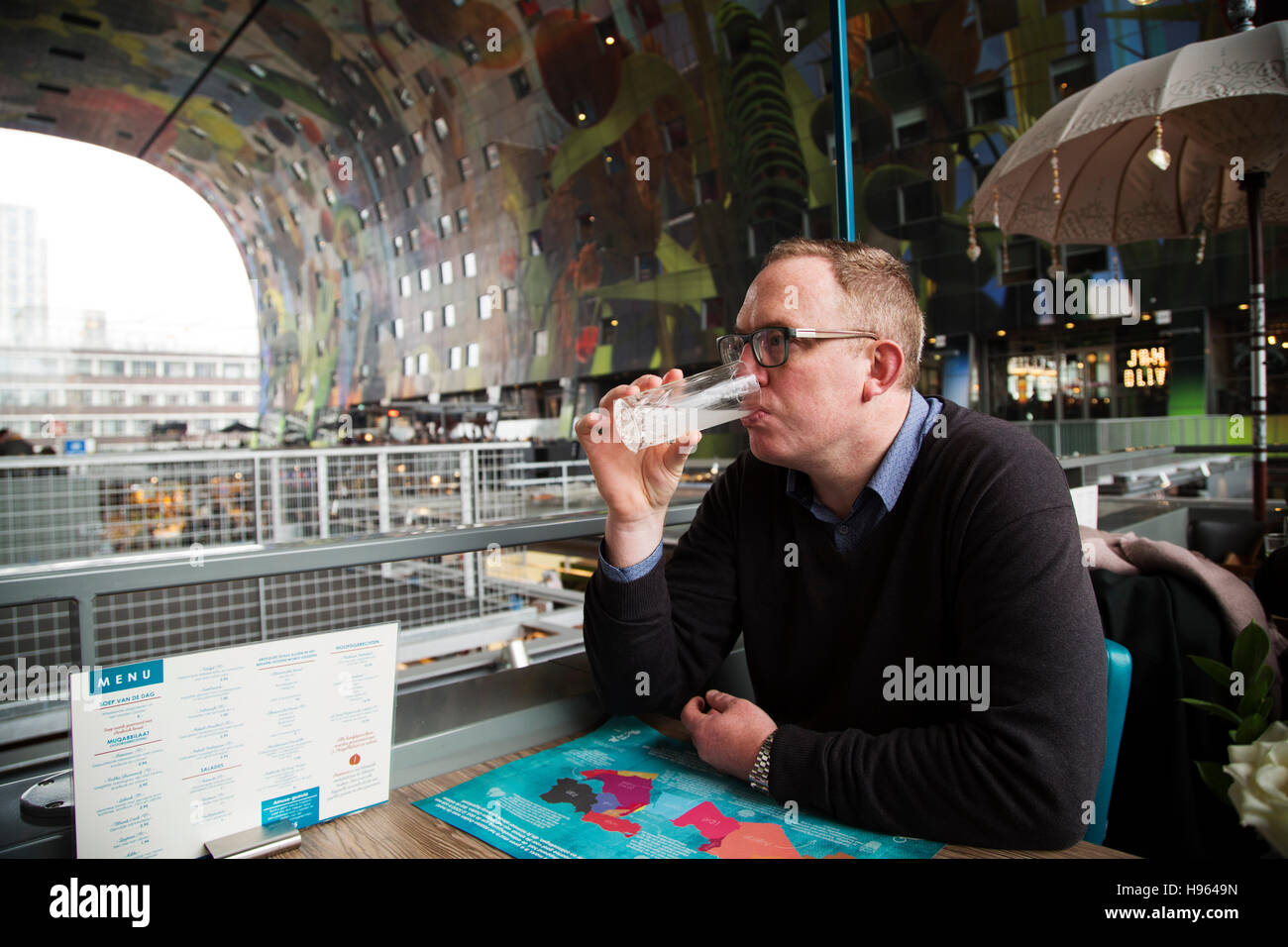 Ein Mann trinkt eine Limonade in einem Restaurant in Markthal in Rotterdam, Niederlande. Die Markthalle und Apartment-Komplex wurde im Jahr 2014 eröffnet. Stockfoto
