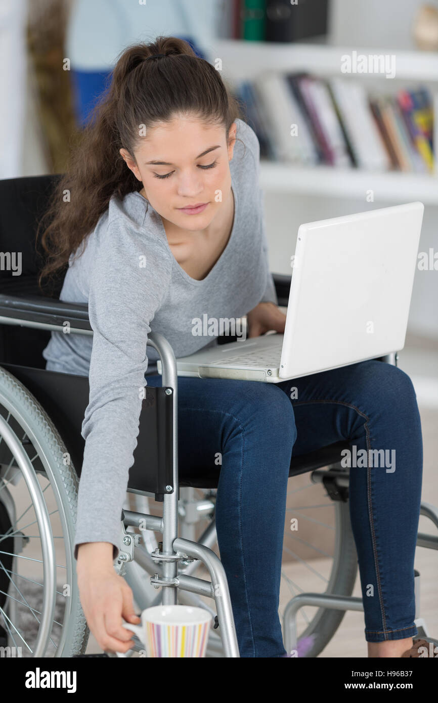 behinderte Frau hält eine Tasse mit ihrem laptop Stockfoto