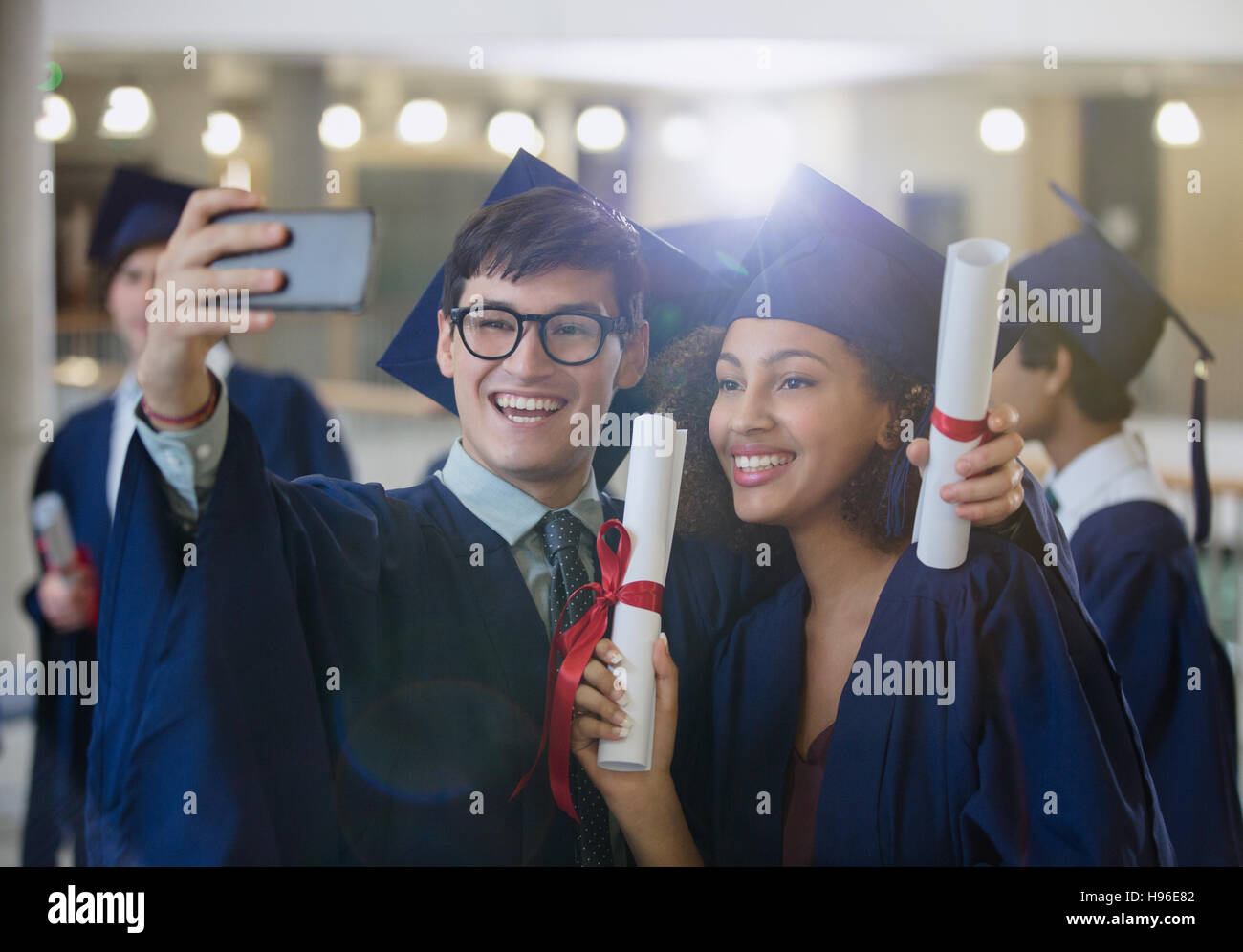 College-Absolventen in Mütze und Mantel hält Diplome posieren für selfie Stockfoto