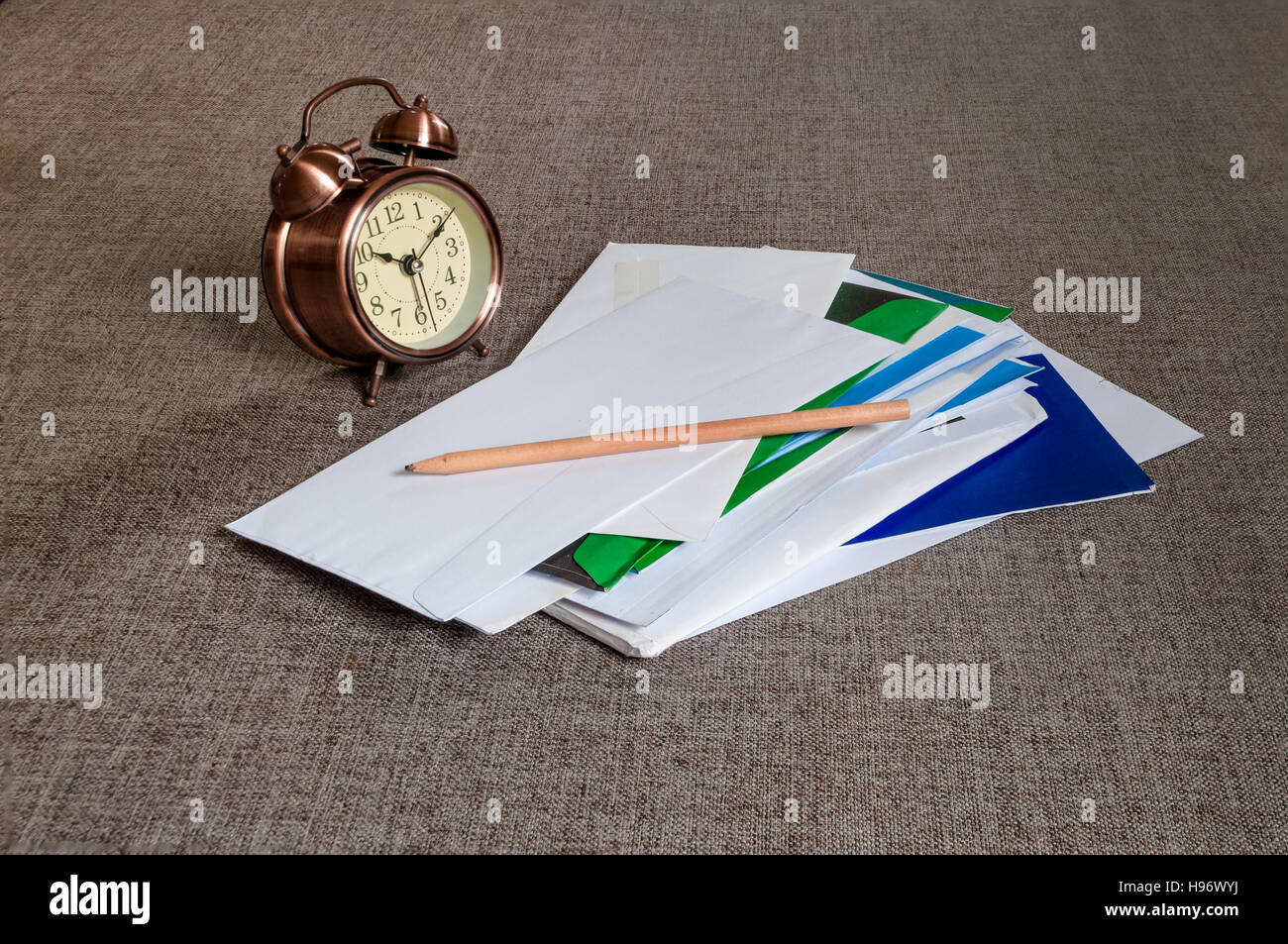 Braune Vintage Uhr, ein Haufen von Post und einen Bleistift auf graue Couch Stoff. Stockfoto