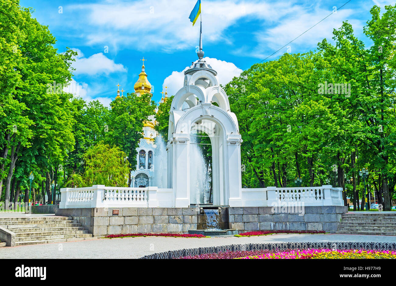 Die weiße Nische auf dem Siegesplatz mit dem Spiegelbrunnen und den hellen goldenen Kuppeln der Kirche der Heiligen Myrrhe-Träger auf dem Hintergrund, Charkiw, Ukraine Stockfoto