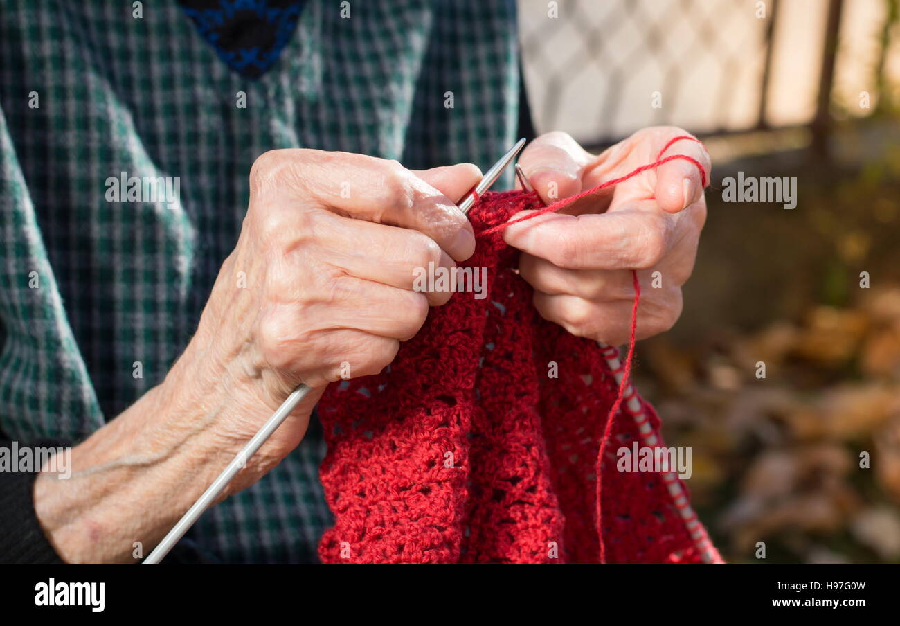 Ältere Frau Hände stricken mit roter Wolle im freien Stockfoto
