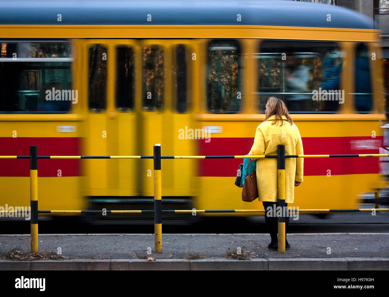 Frau im gelben Mantel und eine gelbe rote Straßenbahn vorbei in Motion blur Stockfoto