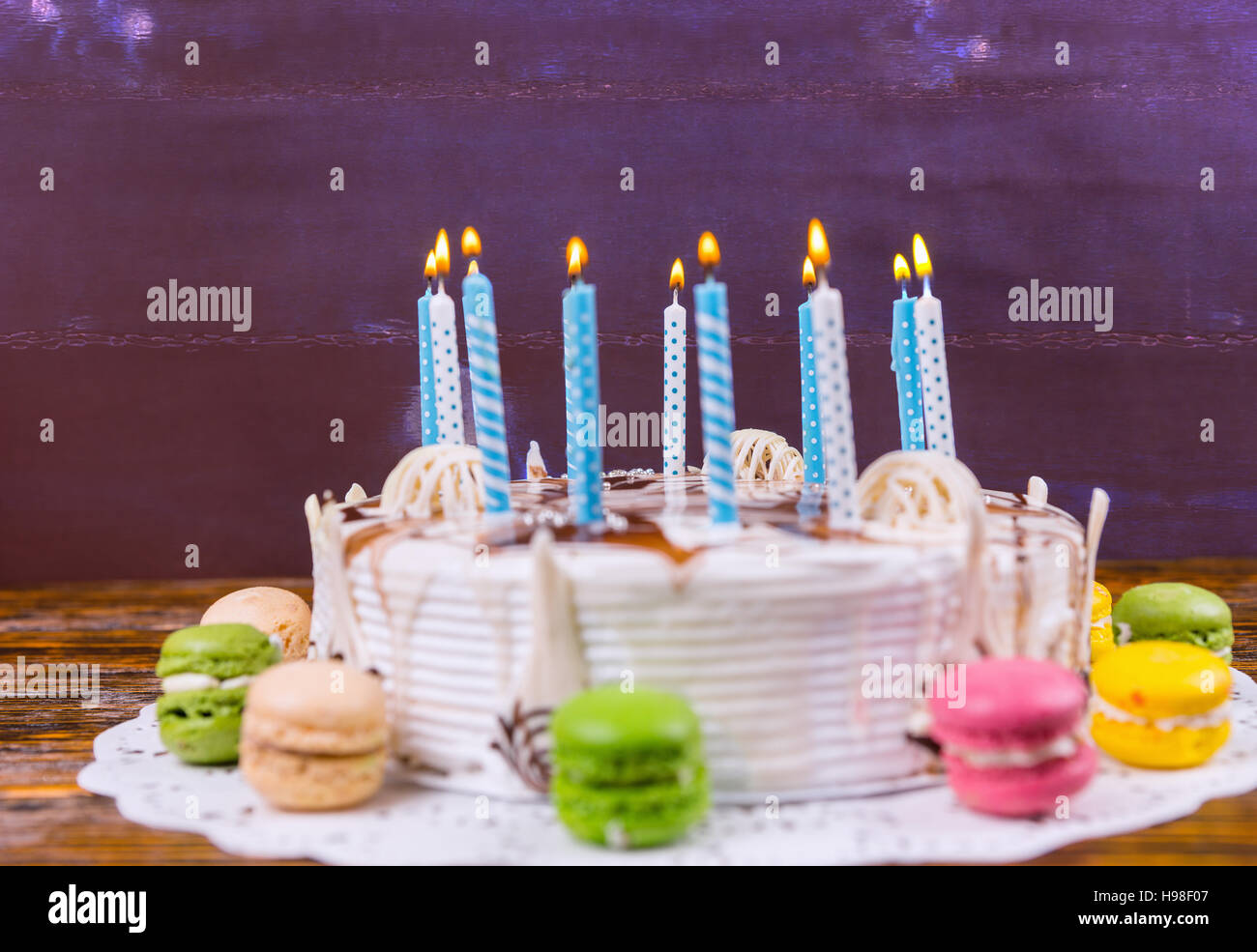 Weiße Geburtstagstorte mit vielen brennenden Kerzen in der Nähe von verschiedenen farbigen