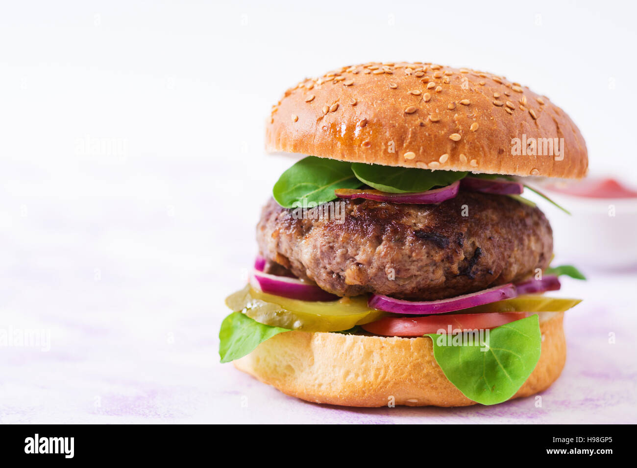 Big Sandwich - Hamburger Burger mit Rindfleisch, Gurken, Tomaten und roten Zwiebeln auf einem hellen Hintergrund. Stockfoto