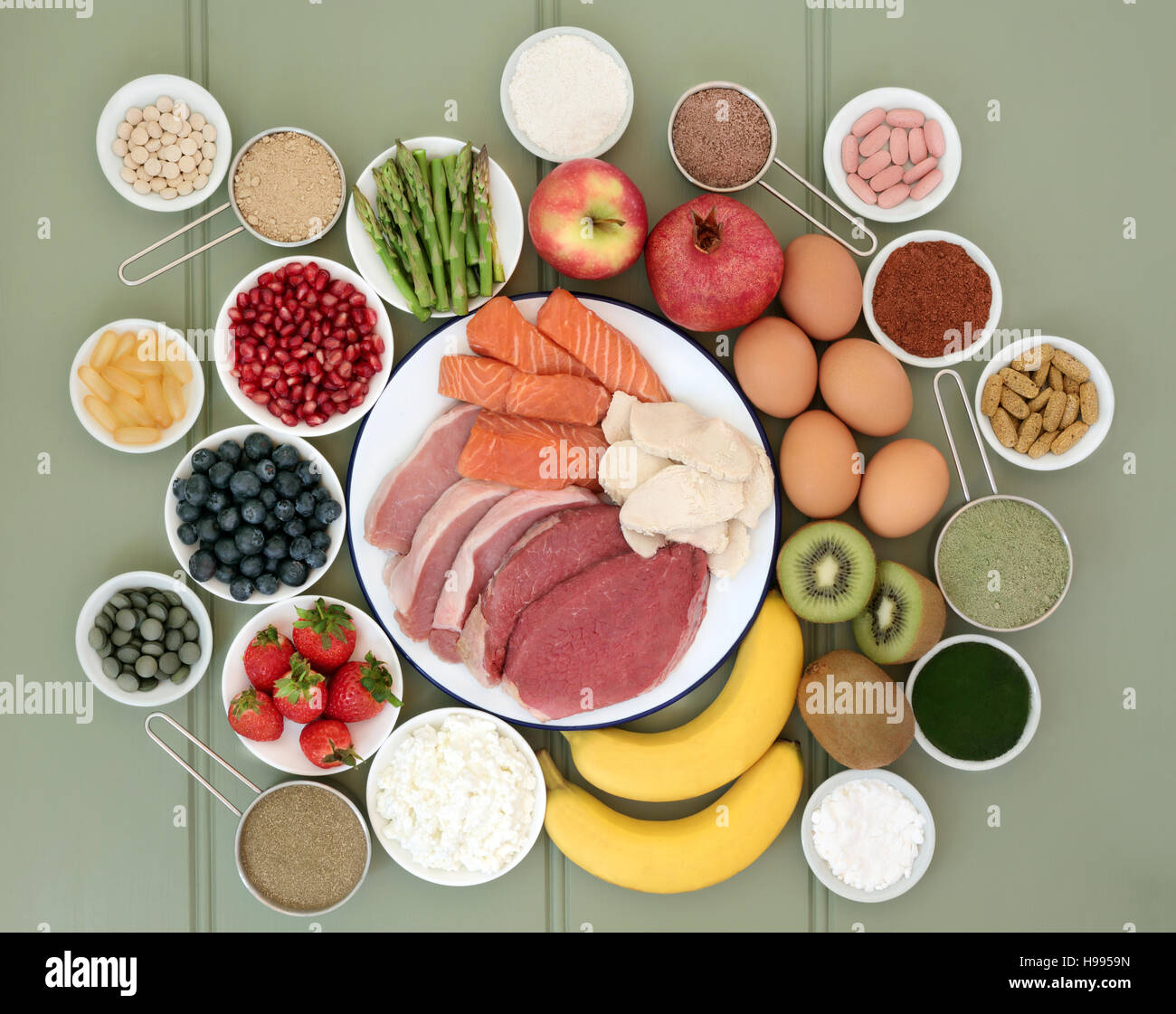 Super Essen für Bodybuilder mit Fleisch, Fisch, Obst, Milchprodukte, diätetische Ergänzung Pulver und Vitamintabletten auf grünem Holz Hintergrund. Stockfoto