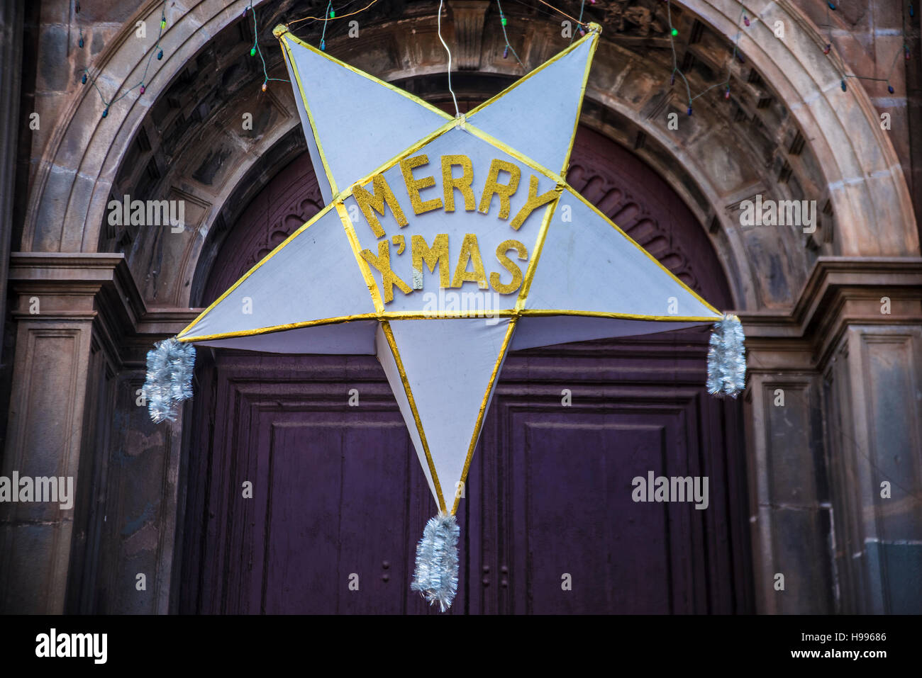 weißer Stern mit merry x-mas-Wörter. Pentagram hängen gegen Kirchentür unter Bogen - Eingang zur Kirche. Frohe Weihnachten in Indien Stockfoto