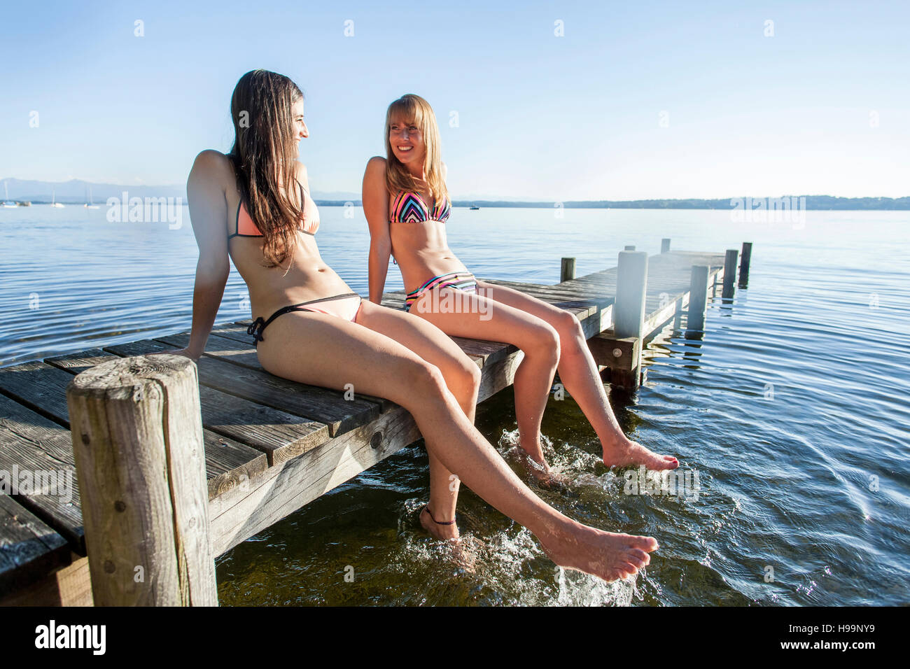 Junge Frauen sitzen auf Pier Spritzwasser mit Beinen Stockfoto