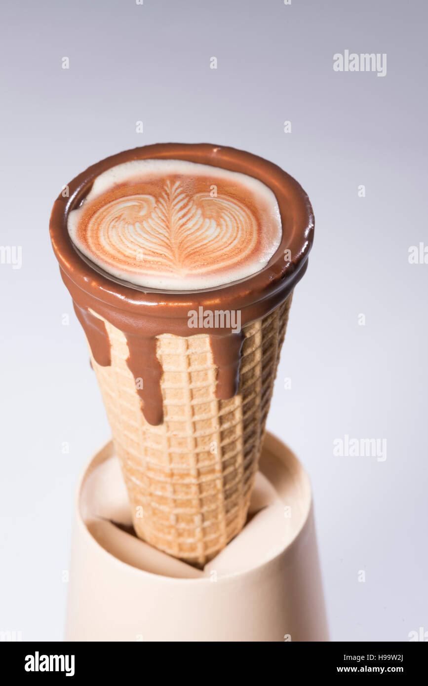 Kaffee im Waffelhörnchen in Schokolade getaucht, mit Zeichnungen in Cappuccino / Latte Milchschaum, Latte Art, isoliert Stockfoto