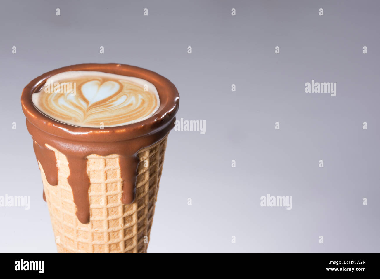 Kaffee im Waffelhörnchen in Schokolade getaucht, mit Zeichnungen in Cappuccino / Latte Milchschaum, Latte Art, isoliert Stockfoto