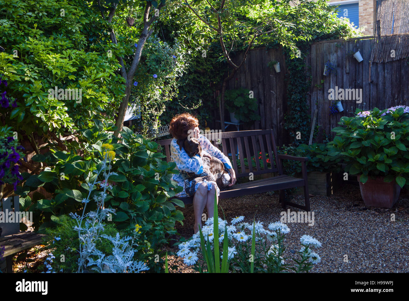 Frauen in Schlafrock sitzen im Garten auf Bank mit einem Hund Stockfoto