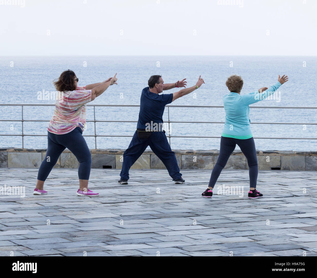 Reifer Mann und zwei Reife Frauen praktizieren Tai Chi mit Blick aufs Meer Stockfoto