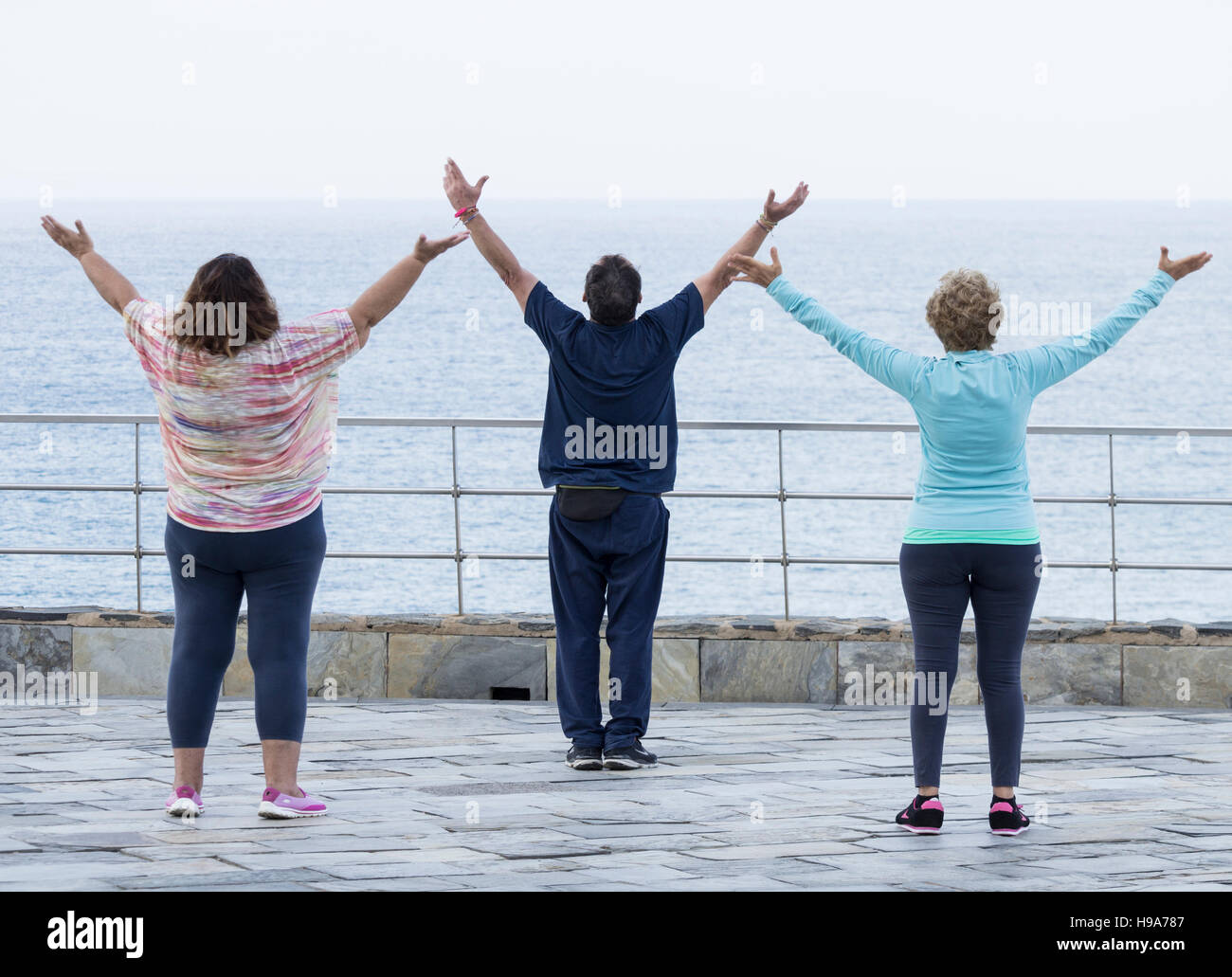 Reifer Mann und zwei Reife Frauen praktizieren Tai Chi mit Blick aufs Meer Stockfoto