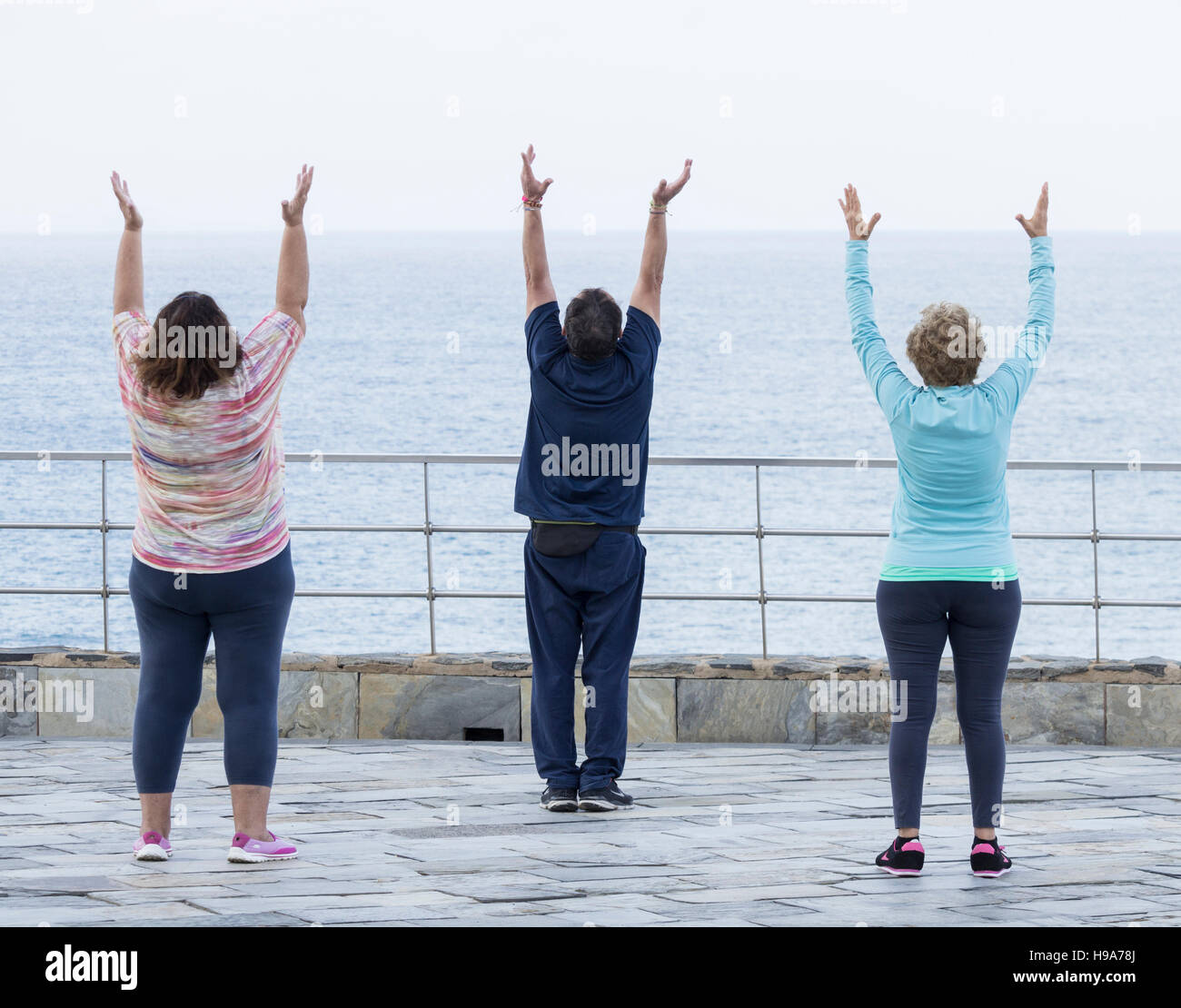 Reifer Mann und zwei Reife Frauen praktizieren Tai Chi mit Blick aufs Meer Stockfoto