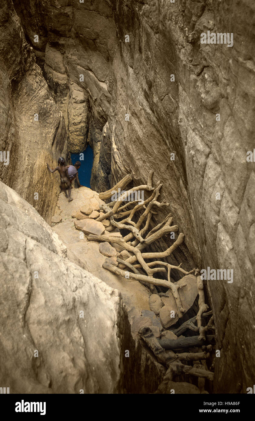 Tireli, Mali, Afrika - 30. Januar 1992: Dogon Dorf und typischen Schlamm Gebäude, Kinder, Wasser in den tiefen Brunnen zu sammeln Stockfoto