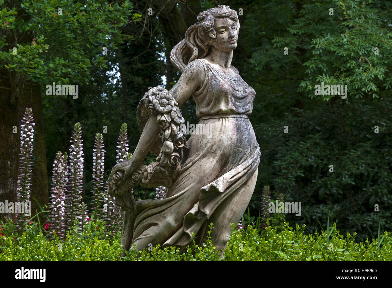 Weibliche Skulptur mit einer Bandbreite von Blumen hinter Akanthus (Acanthus), Parc Floral et tropischen De La Court d'Aron Stockfoto