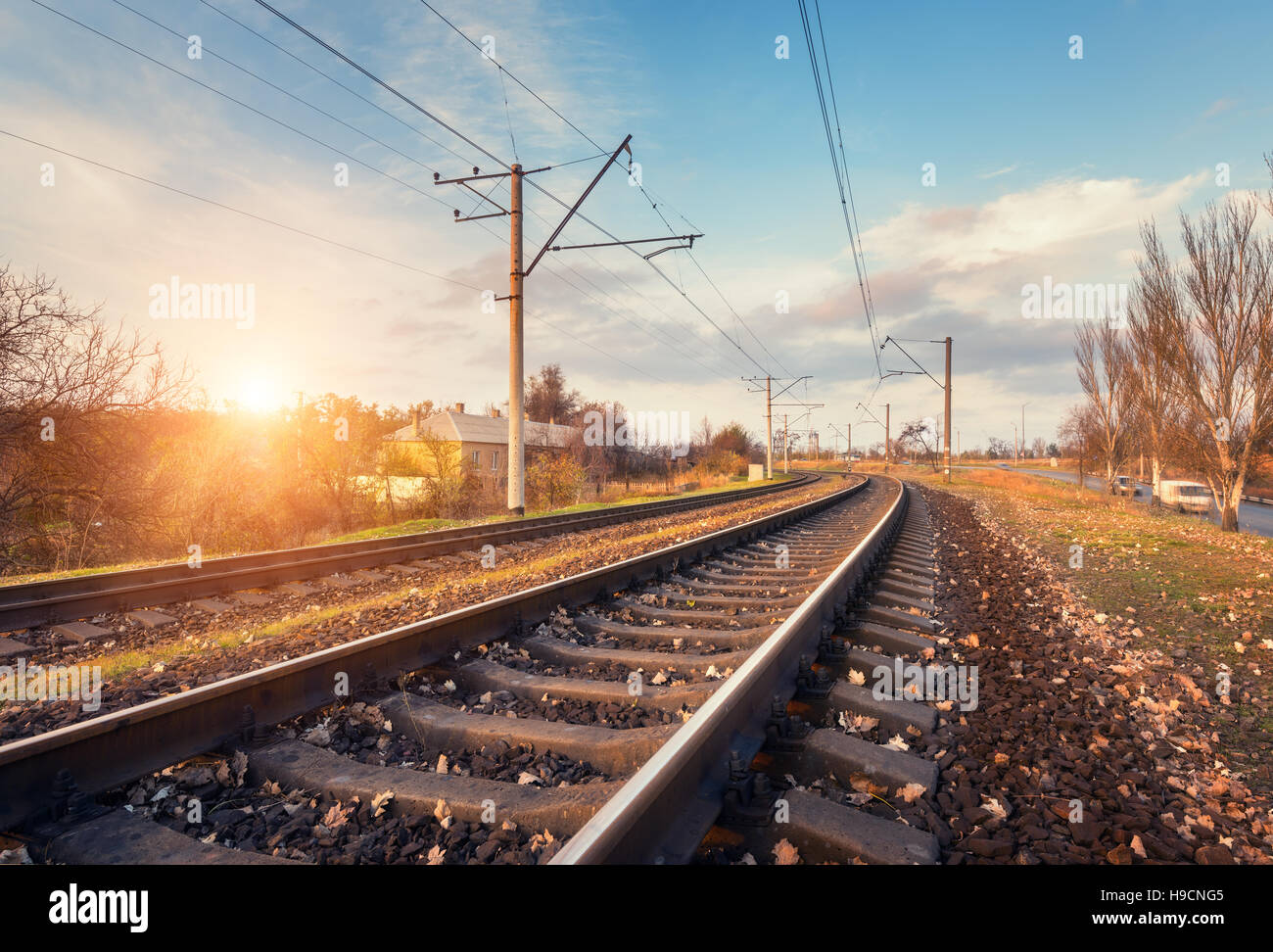 Bahnhof gegen schönen Himmel bei Sonnenuntergang. Industrielandschaft mit Eisenbahn, blauer Himmel mit Wolken, Sonne, Bäume und Rasen. Eisenbahnknotenpunkt Stockfoto