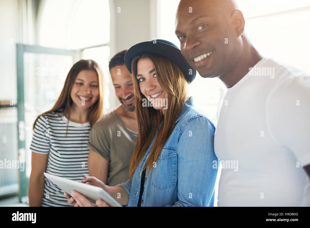 Junge trendige lächelnd Gruppe von vier Freunden mit Tablet Spaß und Blick in die Kamera im Sonnenlicht. Stockfoto
