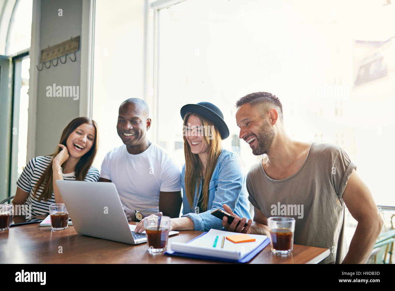 Vier junge lächelnde Mitarbeiter sitzen am Desktop und Laptop in hellen Raum zu betrachten. Stockfoto