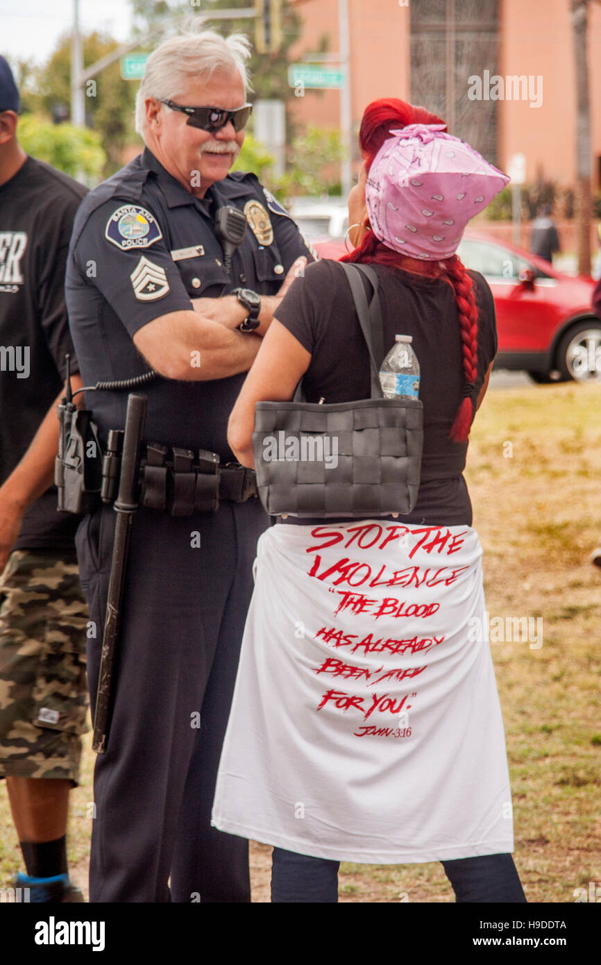 Weibliche junge Hispanic Erwachsene plaudert mit einem lokalen Polizisten bei einer Anti-Gewalt-Rallye in Santa Ana, CA, Stadtpark. Hinweis T Shirt mit Demo-Logos. Stockfoto