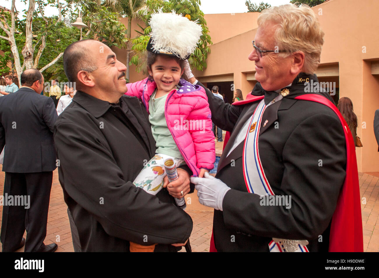 Ein kleines Mädchen in des Vaters Armen versucht die gefiederte Hut ein aufwändig kostümierten Mitglied der Knights Of Columbus nach dem Gottesdienst in der St. Timothy katholische Kirche, Laguna Niguel, CA. Stockfoto