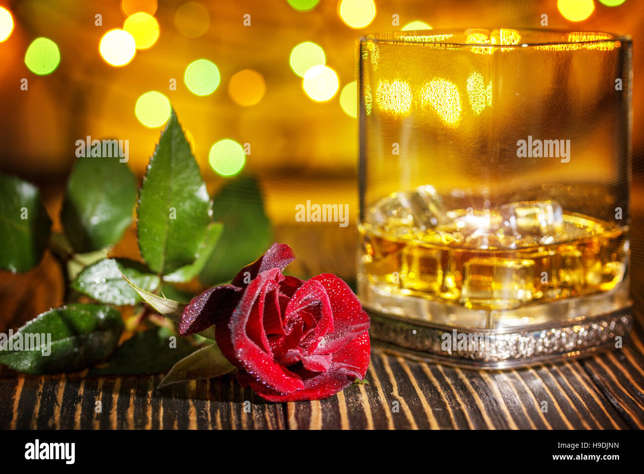Glas Scotch Whisky und Eis, rote rose im Urlaub bunten Bokeh Hintergrund auf Holztisch Stockfoto