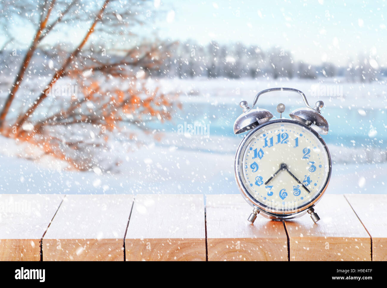 Vintage Wecker auf Holztisch oder Bank bei Schneewetter auf Winter Saison Hintergrund. Zurück zur Winterzeit. Herbstzeit zurück. Tageslicht-Einsparung-Ende Stockfoto