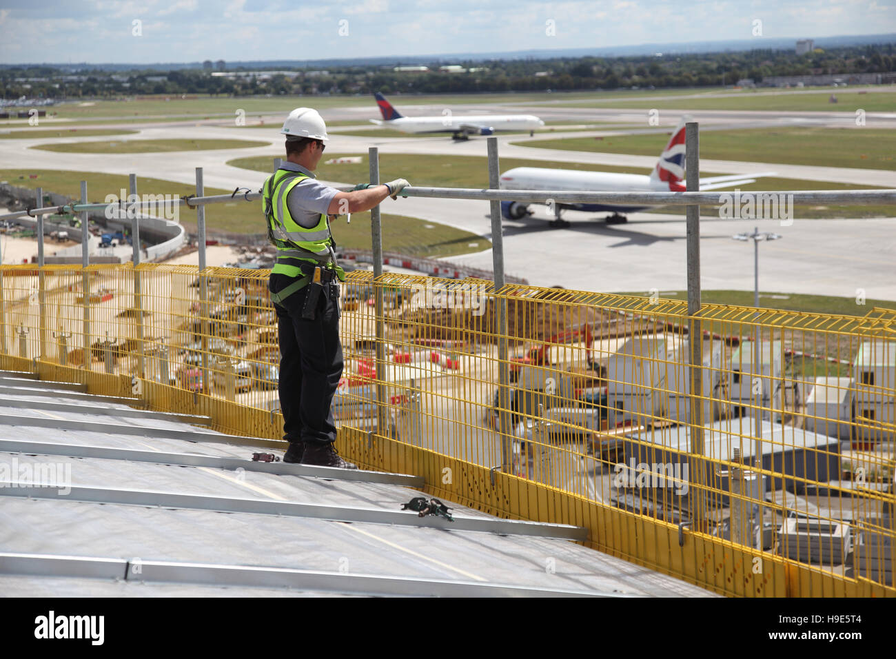 Ein Arbeitnehmer stellt ein Gerüst auf dem Dach des neuen Terminal 2 am Flughafen London Heathrow. Flugzeuge-Taxi im Hintergrund. Stockfoto