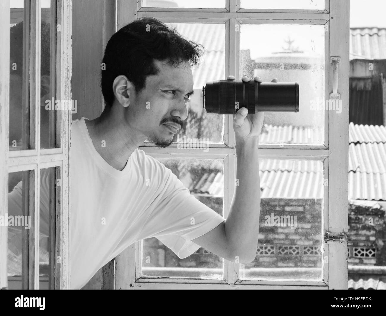 Mann mit Blick durch ein Fenster mit einem Teleobjektiv. Humorvolle Konzept in der schwarz-weiß-Fotografie. Stockfoto