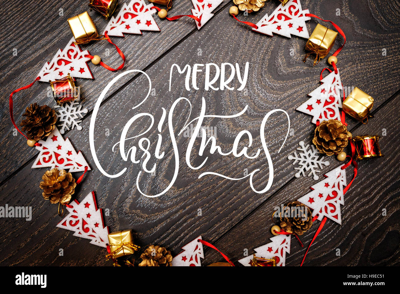 Rahmen von Spielzeug Tannen auf hölzernen Hintergrund und Text Frohe Weihnachten. Kalligraphie-Schriftzug Stockfoto