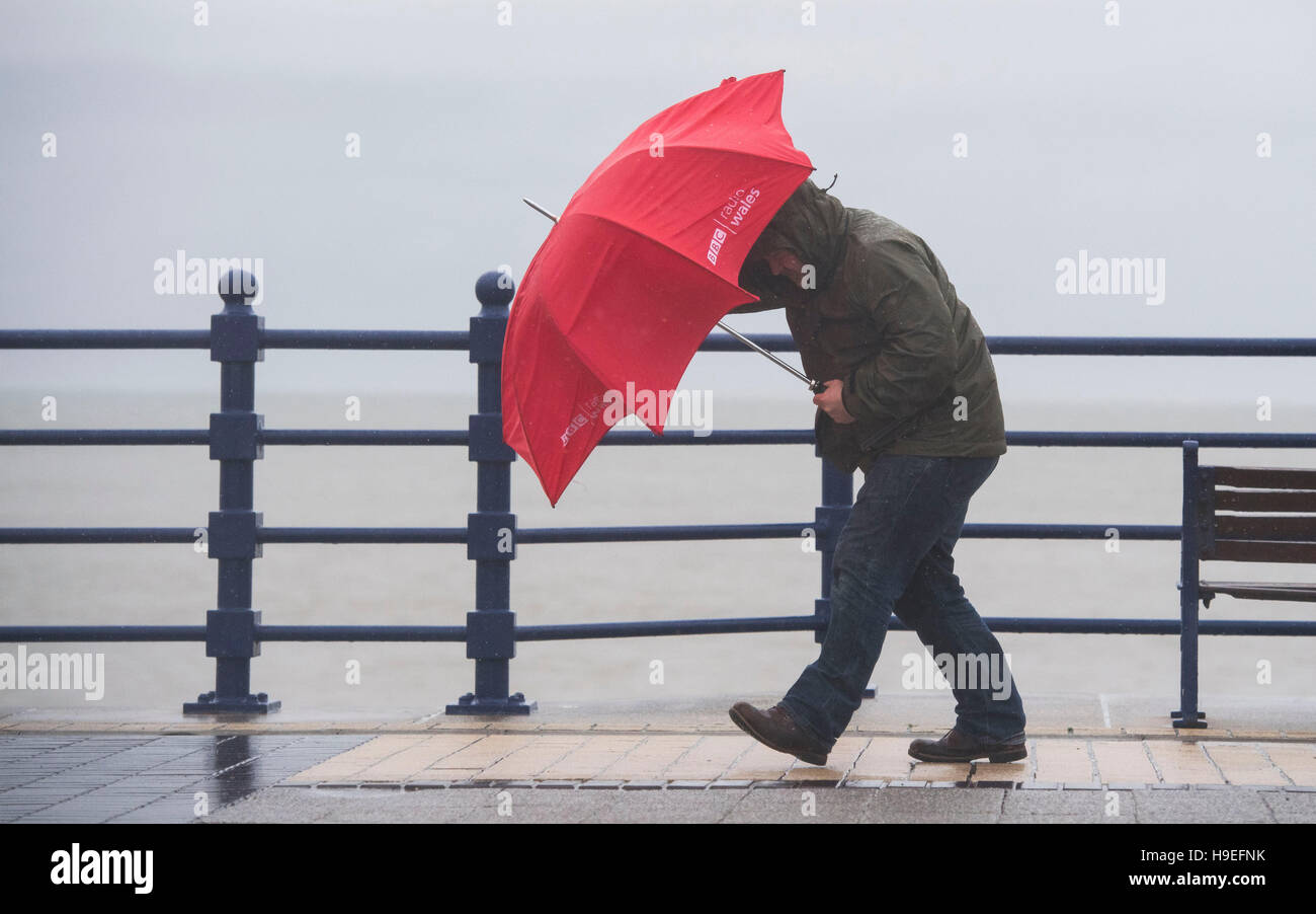 Ein Mann Schlachten starken Winden mit einem roten Regenschirm bei Sturm Angus in Porthcawl, South Wales, UK. Stockfoto