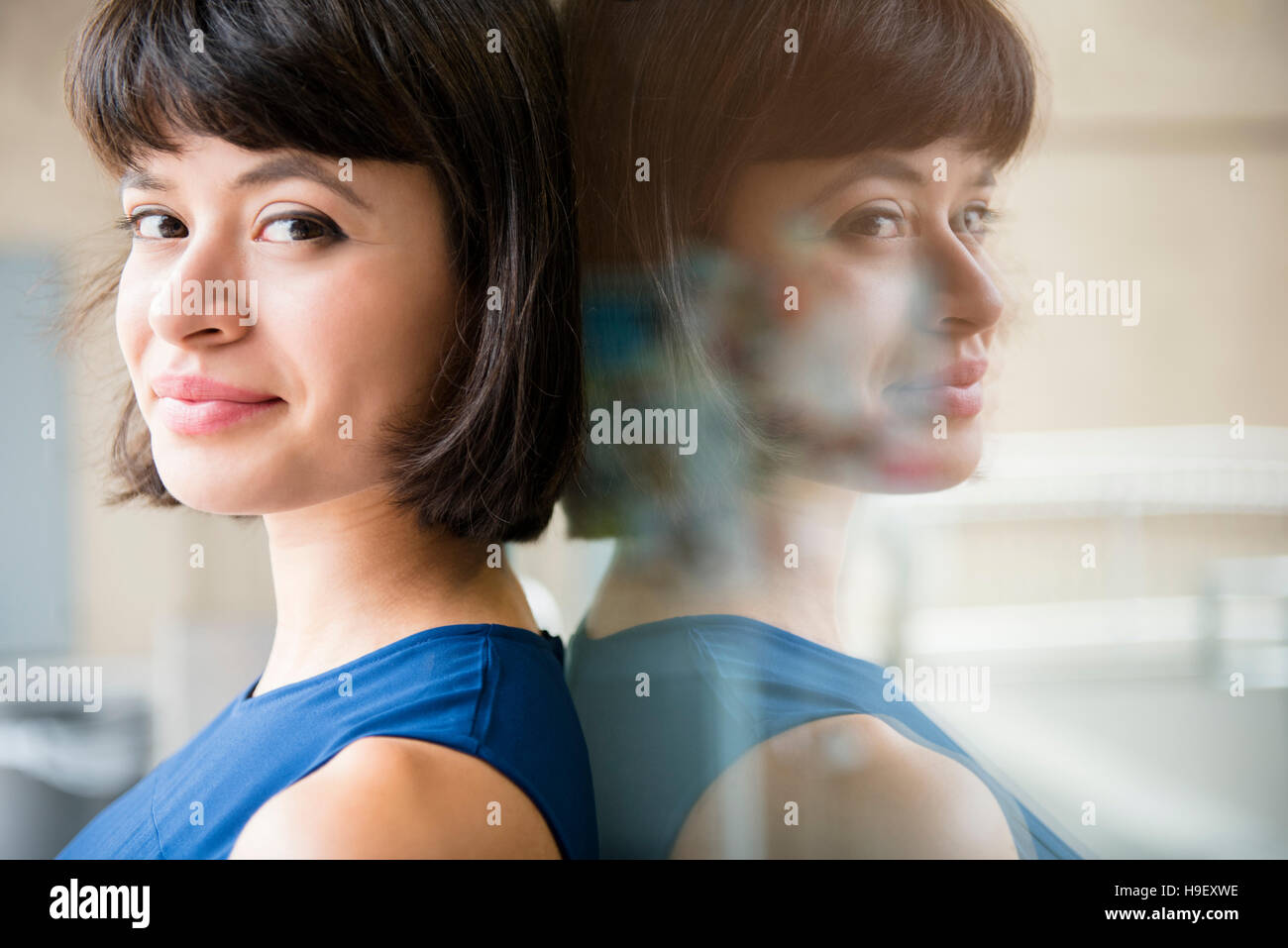 Reflexion der Hispanic Frau lehnt sich an Glaswand Stockfoto