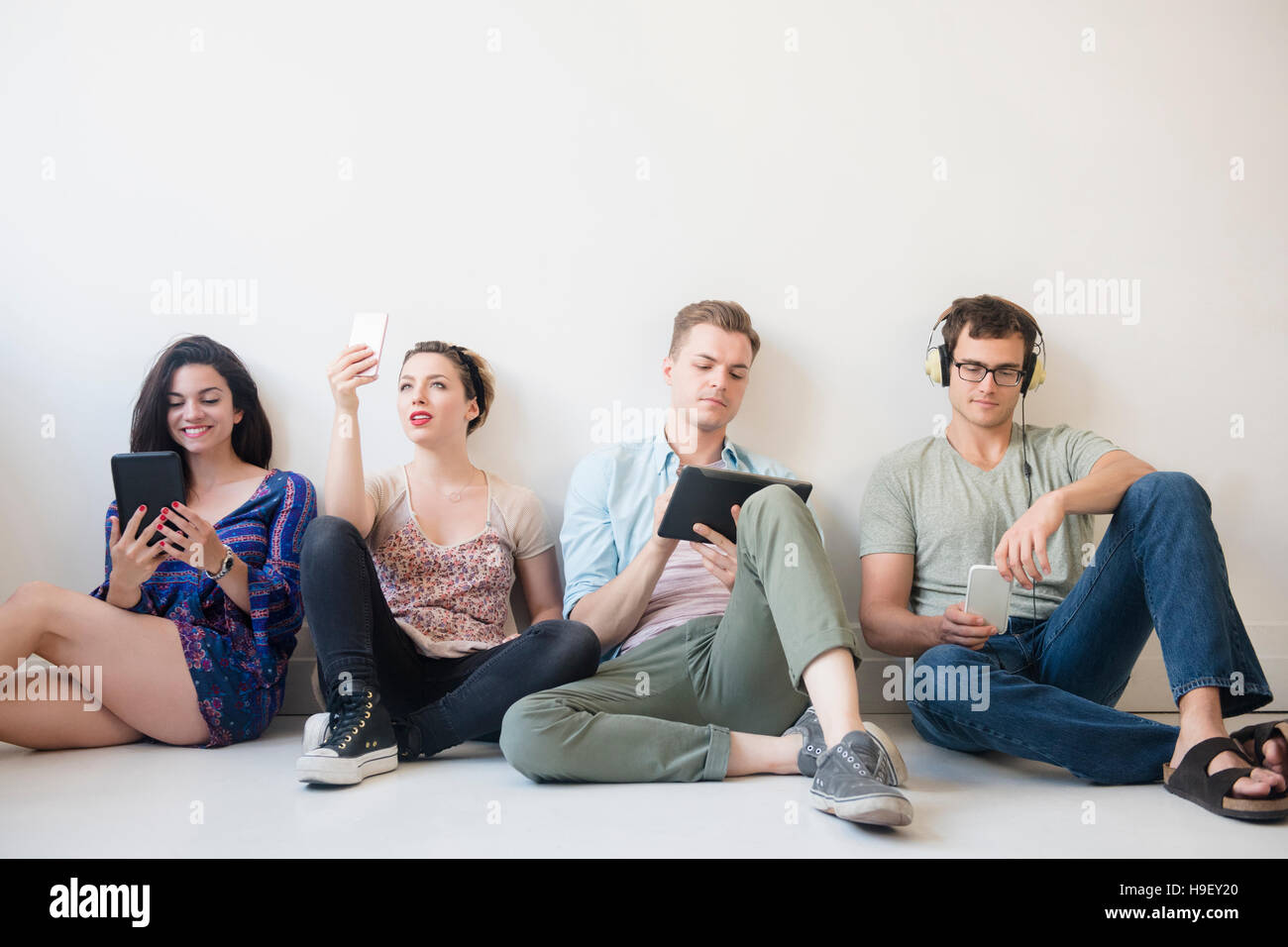 Kaukasische Freunde sitzen auf Boden-Technologie Stockfoto