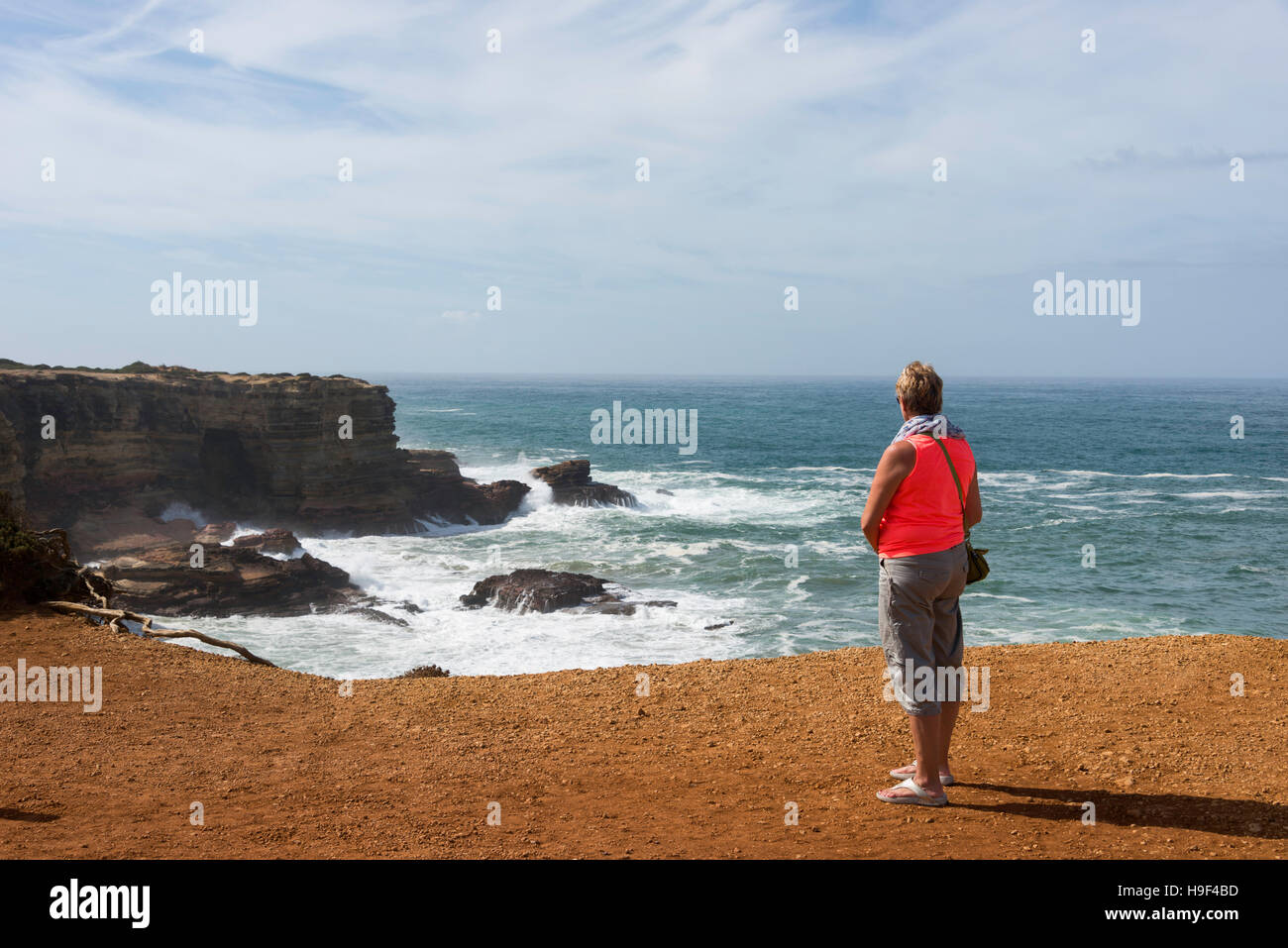 blonde Frau in orange Hemd Blick auf die Wellen an der Küste von Portugal in Alentejo Stockfoto