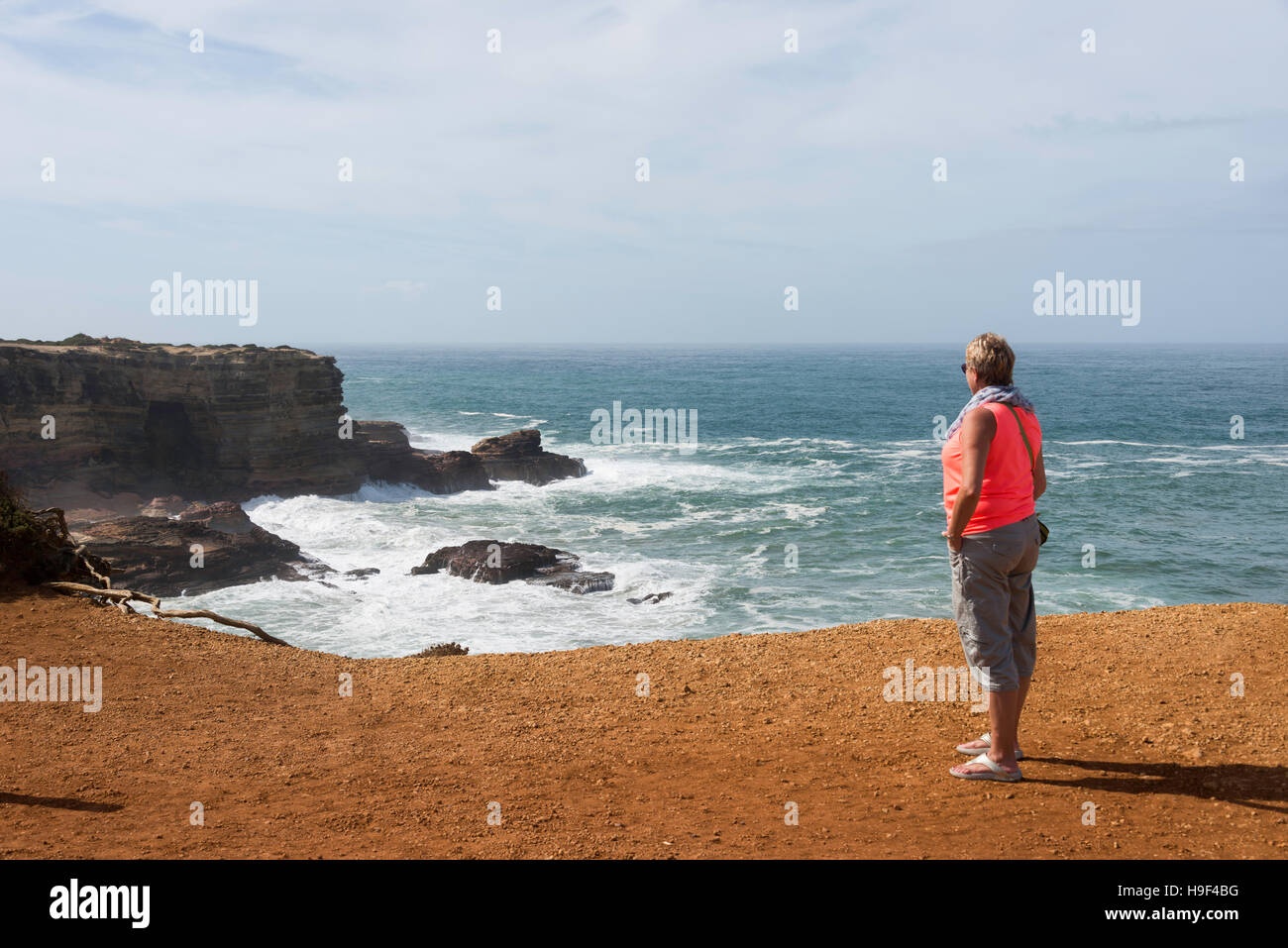 blonde Frau in orange Hemd Blick auf die Wellen an der Küste von Portugal in Alentejo Stockfoto