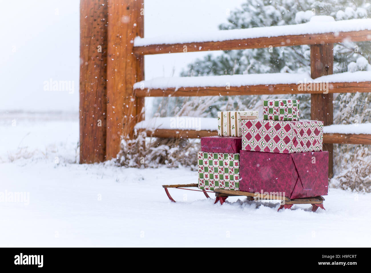 antiker Schlitten mit Geschenken in den Schnee des Landes entlang Holzzaun mit Pinien Stockfoto