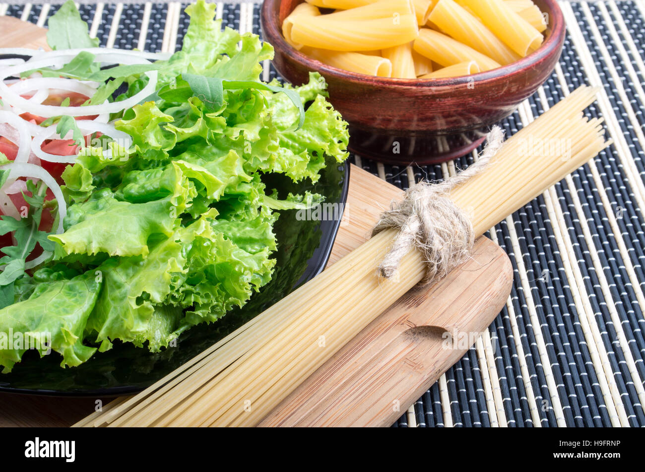 Frischer grüner Salat auf einem Tisch neben den Zutaten für Kochen Nudeln und Spaghetti hautnah Stockfoto
