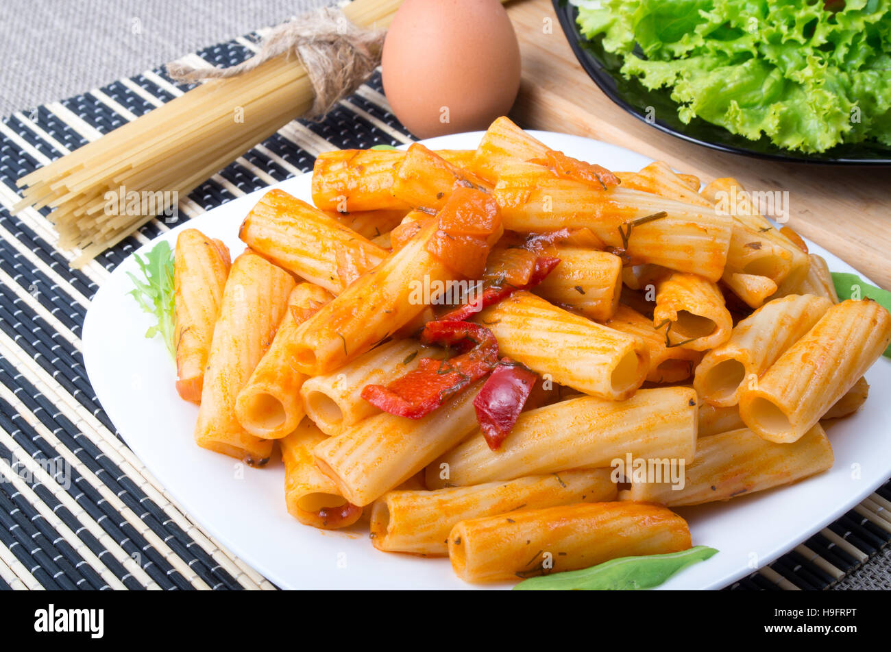 Teller Rigatoni Nudeln mit Gemüsesauce neben den Teller mit Salat und Zutaten zum Kochen Stockfoto
