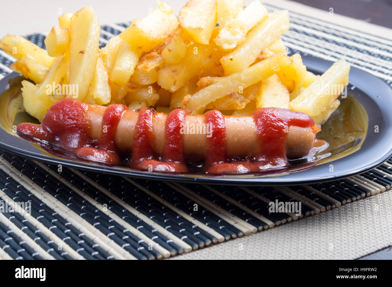 Typisches russisches Gericht Closeup - Bratkartoffeln und Bratwurst mit Tomaten-Ketchup auf einem dunklen Teller Stockfoto
