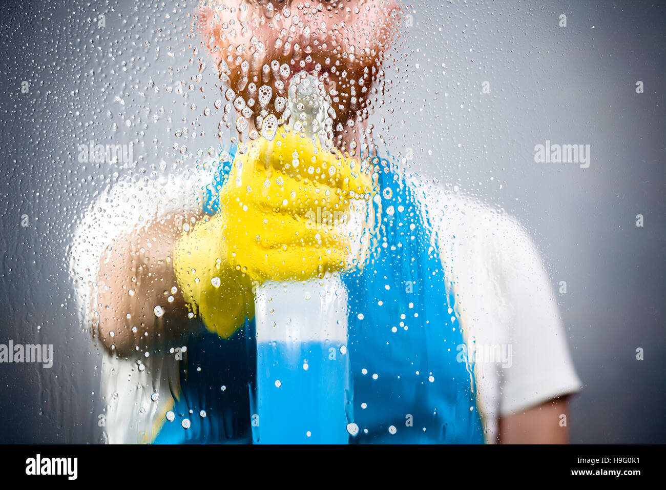 Sauberer Mann spritzen ein Waschmittel, eine Schürze und Plastikhandschuhe tragen Stockfoto