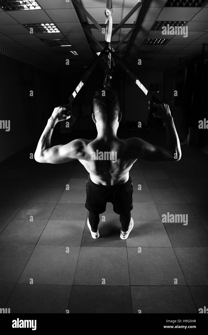 Einen schöner junger tapferer lockiger bärtiger bemuskelt Mann mit einem Bart macht Gesamtwiderstand Übungen Fitness Trx Bändern trainieren Sie im Fitness-Studio Stockfoto