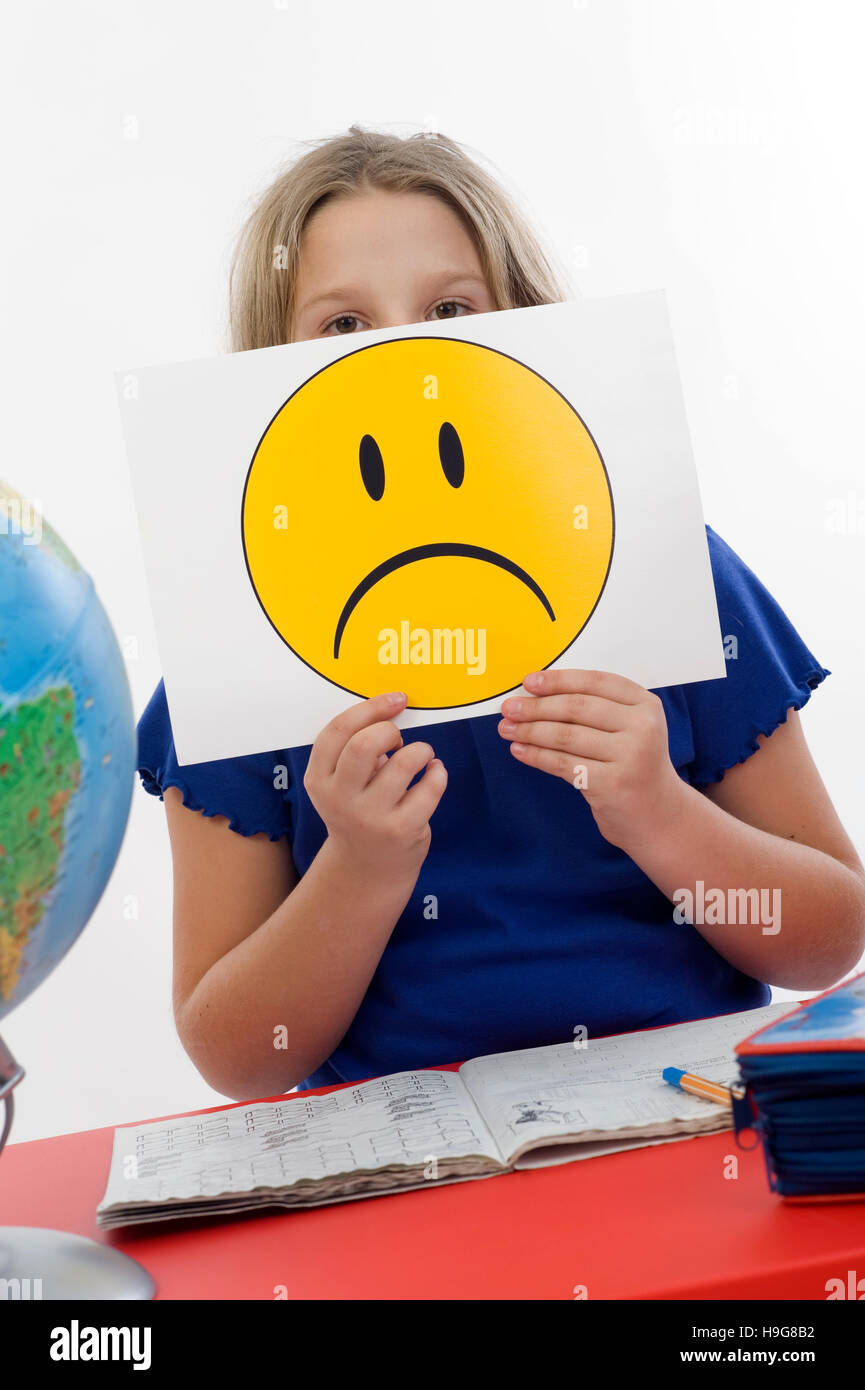 Mädchen an einem Schreibtisch, trauriger Smiley, symbolisches Bild für Probleme in der Schule Stockfoto