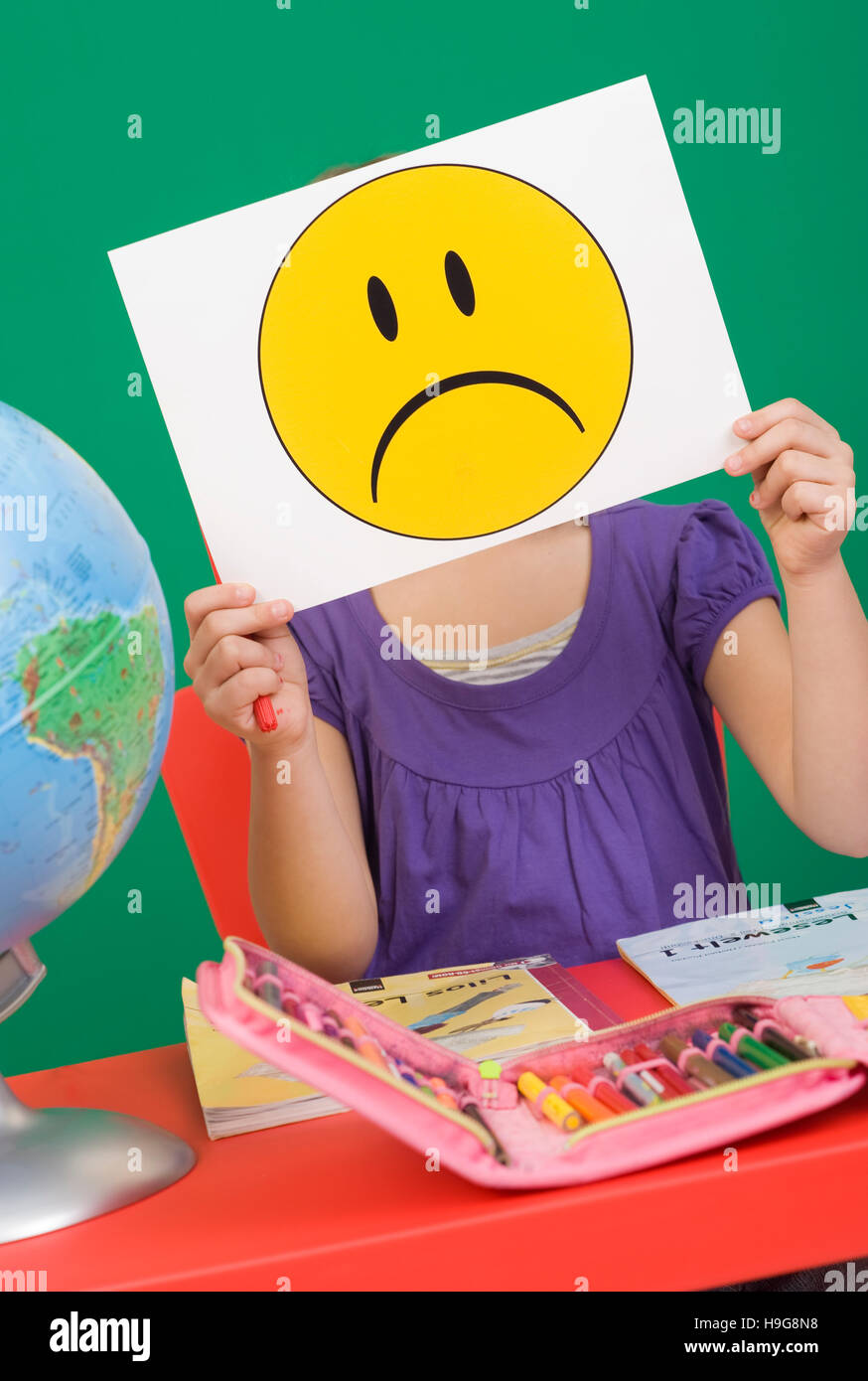 Mädchen an ihrem Schreibtisch, trauriger Smiley, symbolisches Bild für Probleme in der Schule Stockfoto