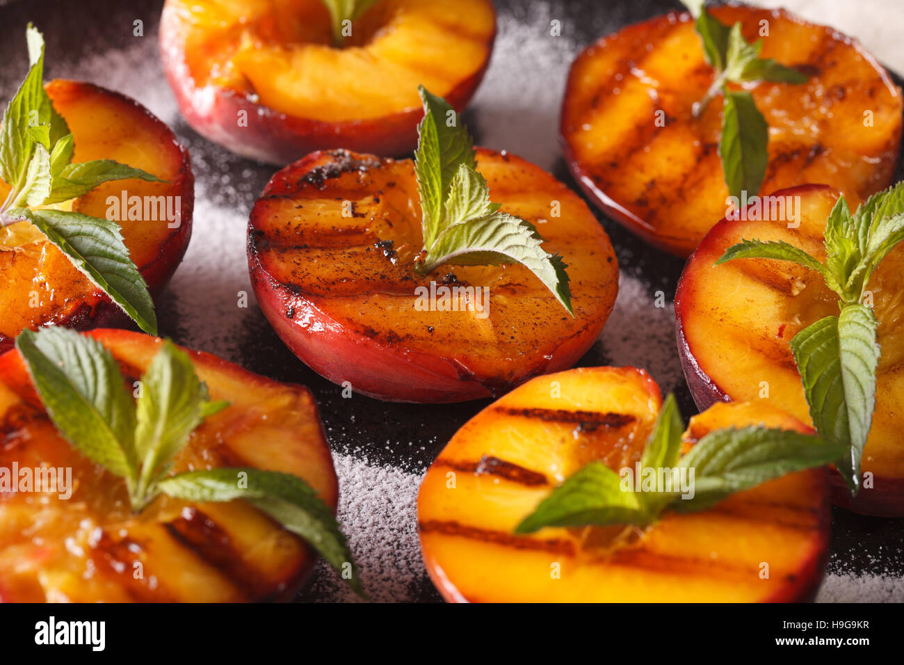 Gegrillte Pfirsiche mit Puderzucker und Minze Makro auf einem Teller. Horizontale Hintergrund Stockfoto