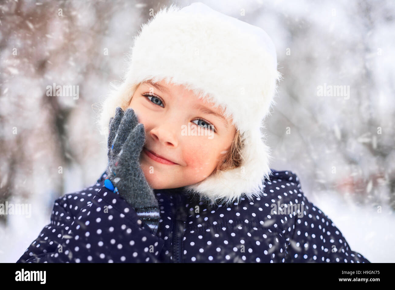 Porträt eines süßen kleinen Mädchens in einem verschneiten Park während eines Schneefalls. Stockfoto