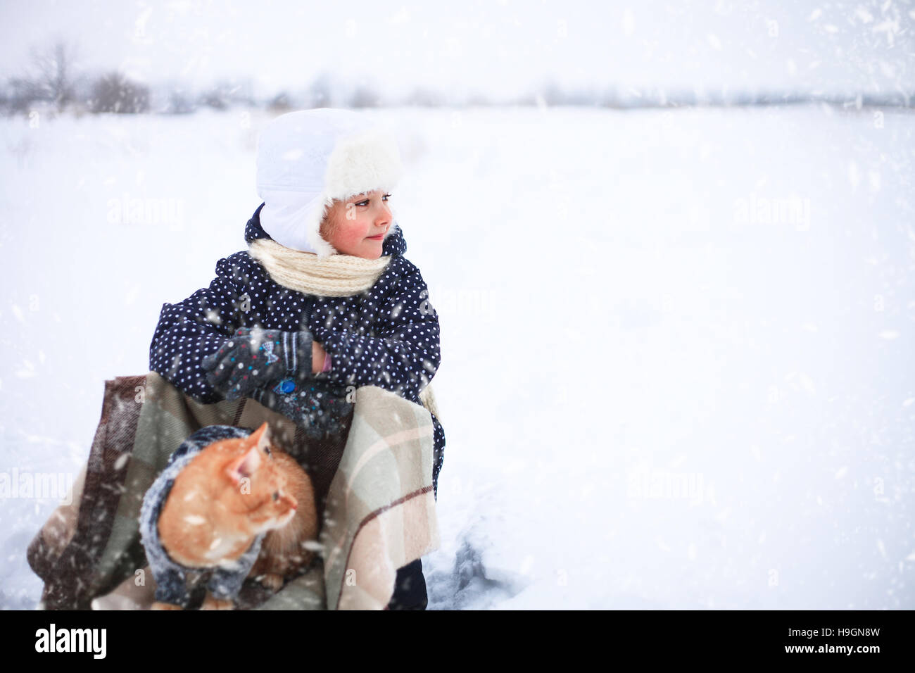 Kleine Mädchen und eine rote Katze auf einem Schlitten fahren in der Landschaft. Stockfoto
